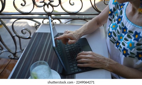 Closeup view of mature senior womans hands using a laptop tablet computer with a drink on a table at cafe on balcony in europe. Traveling digital nomad concept. - Powered by Shutterstock