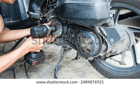 A close-up view of a mechanic's hands using a power wrench to repair the engine of a scooter. Mechanic Repairing a Scooter or motorcycle background.