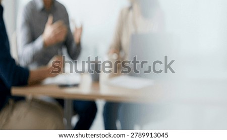 A close-up view of a meeting in progress, featuring blurred figures engaged in discussion at a table with papers and a coffee cup present.