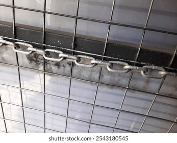 Close-up view of a metal grate or wire mesh structure covered in a layer of dust or debris, creating a slightly grimy and aged appearance. A chain or metal link is visible running across the center. - Powered by Shutterstock