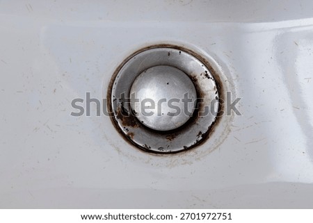 Close-up view of a metallic drain cover in a white sink, showcasing scratches and rust. This image emphasizes wear and tear, useful for home maintenance or renovation contexts.