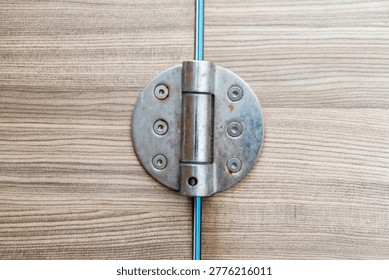 A close-up view of a metallic hinge attached to a wooden surface, highlighting the industrial design and functional role in connecting and supporting structures.