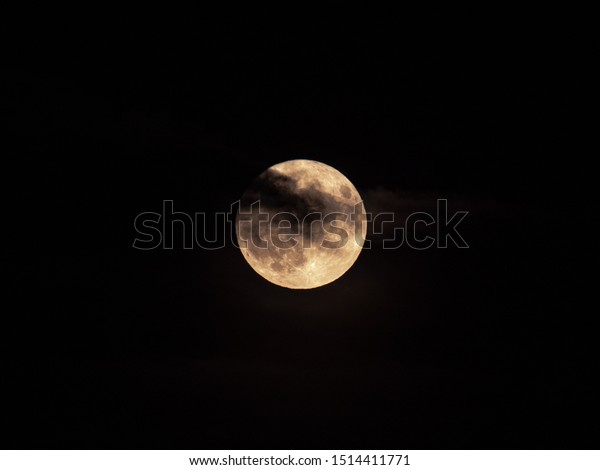 A\
closeup view of the micro harvest moon with partial cloud cover and\
haze on Friday the 13th as seen in Chicago on a black night sky\
backdrop making for a creepy, spooky or scary\
scene.