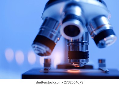Close-up view of a microscope with blue lighting in a laboratory setting.