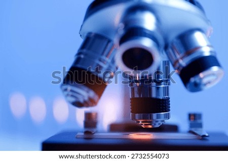 Close-up view of a microscope with blue lighting in a laboratory setting.