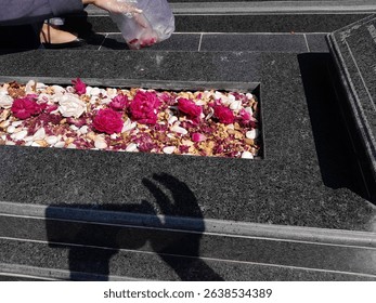 A close-up view of a modern black granite grave adorned with flower petals.  - Powered by Shutterstock - Get 15% off with code: PIKWIZARD15