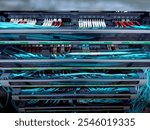 A close-up view of a modern server rack filled with numerous teal fiber optic cables. The cables are neatly organized and connected to various ports. Each rack unit is clearly labeled.