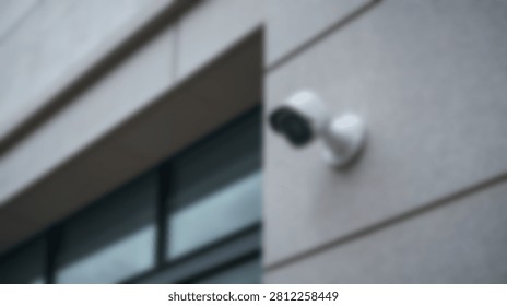 A close-up view of a modern white security camera attached to the exterior wall of a contemporary building.