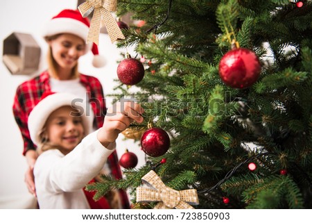 close-up view of mother and daughter decorating christmas tree with shiny baubles