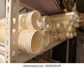 Close-up view of multiple stacks of disposable paper cups, each bundle wrapped in transparent plastic, stored in a restaurant's supply room.