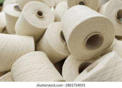 A close-up view of multiple wool yarn spools stacked together, highlighting the texture and material used in weaving and spinning processes in a textile factory.