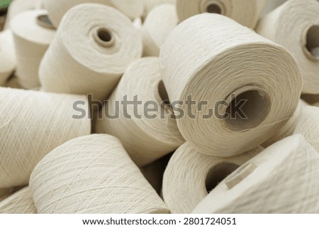 A close-up view of multiple wool yarn spools stacked together, highlighting the texture and material used in weaving and spinning processes in a textile factory.