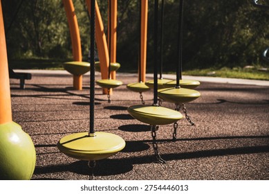 A close-up view of multiple yellow disc swings suspended by ropes from orange poles in a park setting
