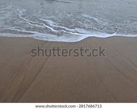 Close-up view of the ocean's edge, showcasing the rhythmic movement of waves washing over golden sand, a serene coastal landscape.
