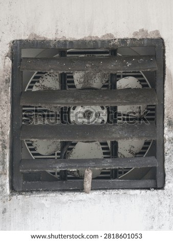 Close-up view of an old grimy wall exhaust fan covered with dust and dirt behind plastic slats