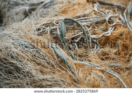 Close-up view of old, weathered, and tangled commercial fishing nets, lines, and ropes, highlighting complex structures and fibers. Ideal as a background or texture for themes related to fishing, maritime trade, coastal heritage, and marine environments.
