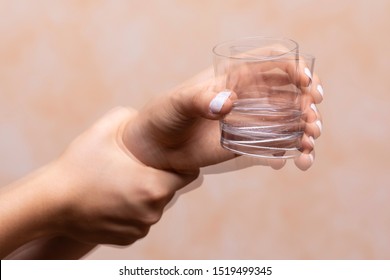 A closeup view on the hands of a person trying to hold a glass of water steady, shaking hands symptomatic of a central nervous and motor system disease such as Parkinson's