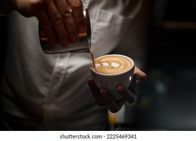 Close-up view on process of pouring of whipped cream from steel jug into cup of coffee in male hand. - Powered by Shutterstock