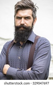 Closeup View Of One Handsome Senior Stylish Man With Black Hair And Long Lush Beard In Blue Shirt Standing Outdoor On White Wall Background, Vertical Picture