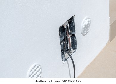 Close-up view of an open electrical box with visible wires and two round ventilation grilles on a textured white wall