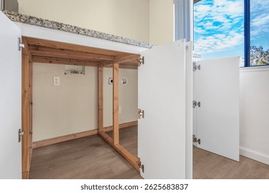 Close-up view of open kitchen lower cabinets revealing exposed framing and utility hookups beneath a granite countertop. Ideal for real estate listings and renovation or construction showcases.