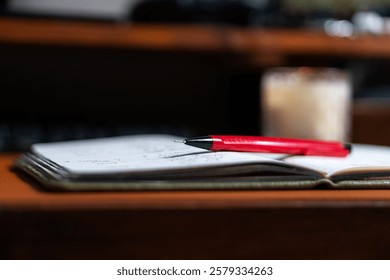 A close-up view of an open notebook with handwritten notes, featuring a red pen resting on the pages. In the background, a blurred candle adds a warm ambiance.