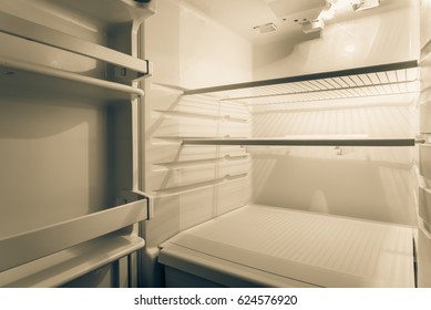 Close-up View An Open Refrigerator With Empty White Shelves, Inside Of Clean Modern Fridge At Night. Lack Of Food, Diet And Hunger, Weight Loss Diet And Unhealthy Eating Disorder Concept. Vintage Tone