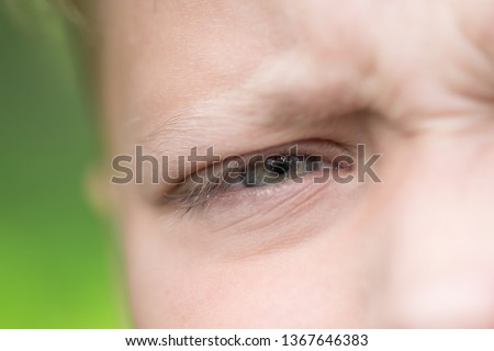 Closeup view of opened eye of blond caucasian young tired frowning boy of school age outside on summer sunny day. Macro horizontal color photography.