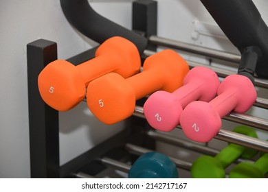 Close-up view of orange and pink dumbbells on metal shelf in sport fitness center. Weight training equipment concept.
					
					5 kg and 2 kg dumbells or barbells.