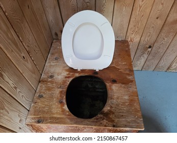 A Closeup View Of An Outhouse Toilet With The Toilet Seat Up.