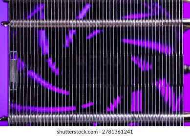 Close-up view of parallel metallic coils arranged with thin vertical wires creating a geometric pattern. Purple light softly illuminates the background, highlighting the industrial texture and reflect