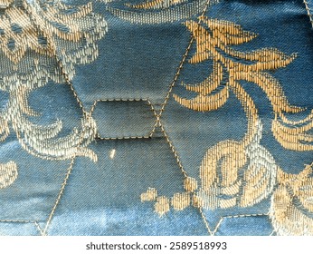 a close-up view of a patterned fabric showcasing a hexagonal design. The fabric features a combination of blue and gold hues, with intricate floral motifs embroidered throughout