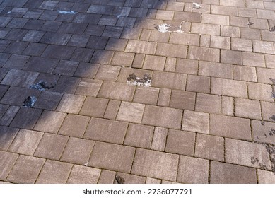 Close-up view of a patterned stone pavement with varying shades and some snow remnants, showcasing texture and shadow play. Ideal for outdoor and architectural themes.