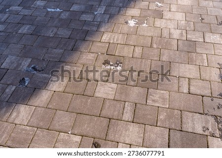 Close-up view of a patterned stone pavement with varying shades and some snow remnants, showcasing texture and shadow play. Ideal for outdoor and architectural themes.