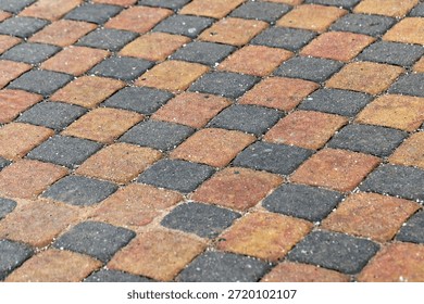 A close-up view of a patterned walkway made from orange, yellow, and gray interlocking paver tiles. The warm tones and geometric layout convey durability, design, and outdoor space elegance