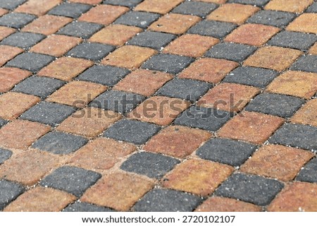 A close-up view of a patterned walkway made from orange, yellow, and gray interlocking paver tiles. The warm tones and geometric layout convey durability, design, and outdoor space elegance