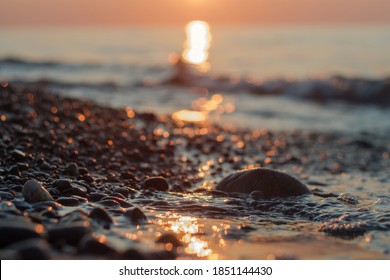 Close-up view of a pebble beach with blurred sea and sun background, selective focus - Powered by Shutterstock