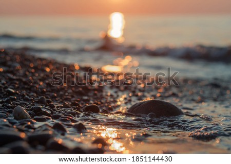 Close-up view of a pebble beach with blurred sea and sun background, selective focus