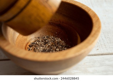 A closeup view of a pepper mill grinding black pepper into a condiment cup. - Powered by Shutterstock