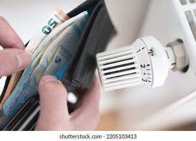 close-up view of person holding wallet with cash next to turned down thermostat on radiator, rising energy and heating costs concept - Shutterstock ID 2205103413