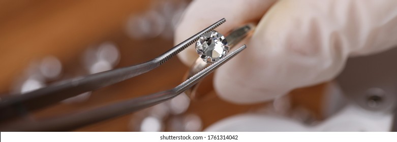 Close-up view of persons hands in protective gloves holding special equipment and examining quality of diamond. Magnifying loupe on table. Luxury jewelry concept