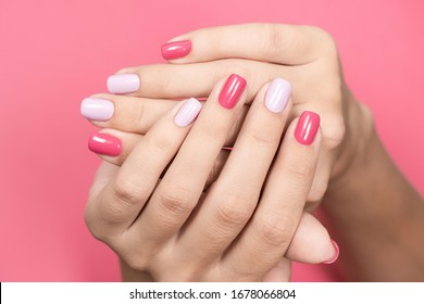 Nahaufnahme von zwei kreuzten schönen weißen Händen der kaukasischen erwachsenen Frau mit angesagter asymmetrischer zwei Farben helle Maniküre einzeln auf pastellrosa Hintergrund. Beauty- und Modekonzept