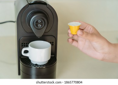 Closeup View Photography Of Woman Holding Coffee Capsule In Hand Ready To Make Cup Of Black Coffee Using Small Black Coffee Machine