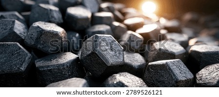 A close-up view of a pile of dark, hexagonal coal briquettes, with a bright sunbeam illuminating the scene from the upper right.