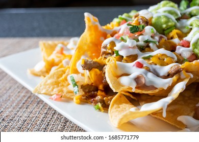 A closeup view of a plate of carne asada nachos, cut off on the right side of the frame, in a restaurant or kitchen setting.