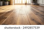 A close-up view of polished wooden flooring in a bright room. Sunlight streams through large windows, casting warm light on the floor.