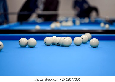 A close-up view of a pool table featuring multiple white billiard balls scattered across a vibrant blue felt surface, with blurred figures in the background