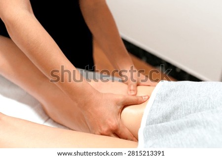 Close-up view of a practitioner performing a therapeutic massage, on a client's lower leg and ankle while the client lies on a treatment table covered with a..