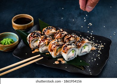 Close-up view of process of preparing rolling sushi. making the sushi with sauce and sesame seeds, pours delicious fresh rolls with a sauce. Dark background - Powered by Shutterstock