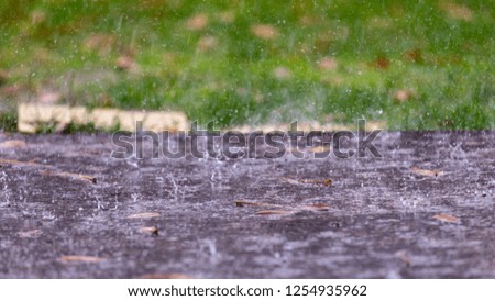 Closeup up view of a rain drops falling on a concrete patio on a background of a house. Large drops create multiple splashes.